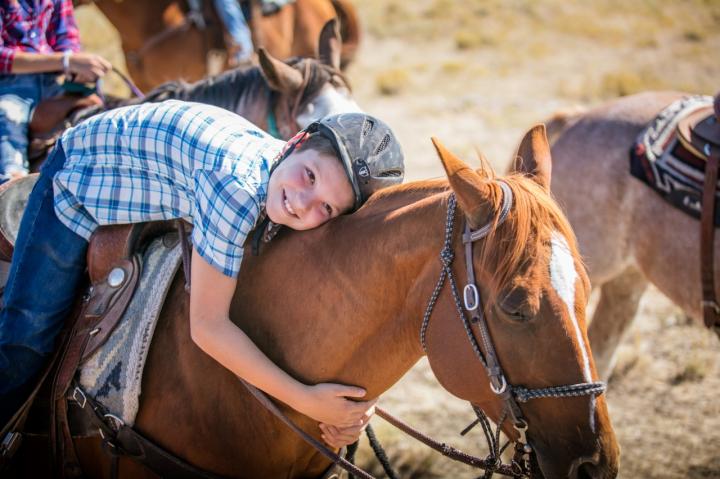 Child hugging horse on ranch vacation