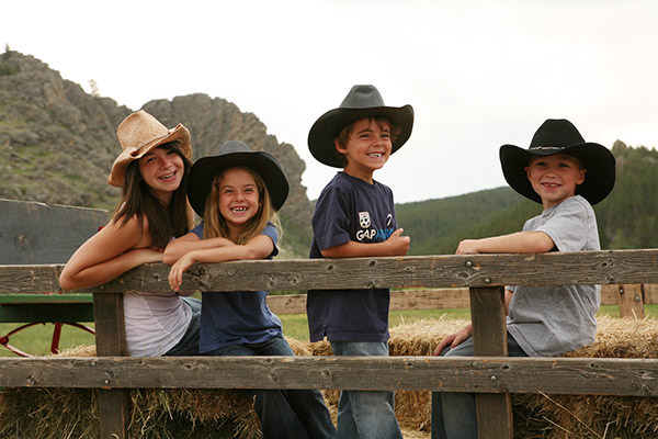 SMiling kids in stetsons leaning on fence